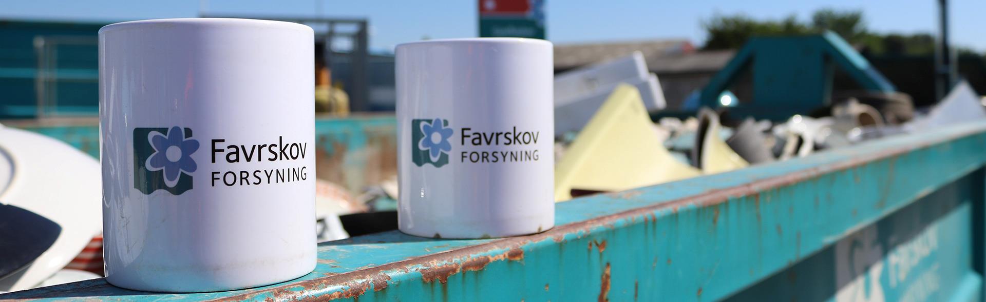To kopper med Favrskov Forsynings logo står på kant af container på genbrugspladsen