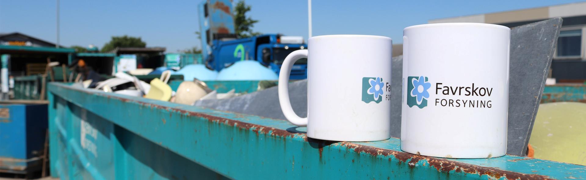 To kopper med Favrskov Forsynings logo står på kant af container på genbrugspladsen