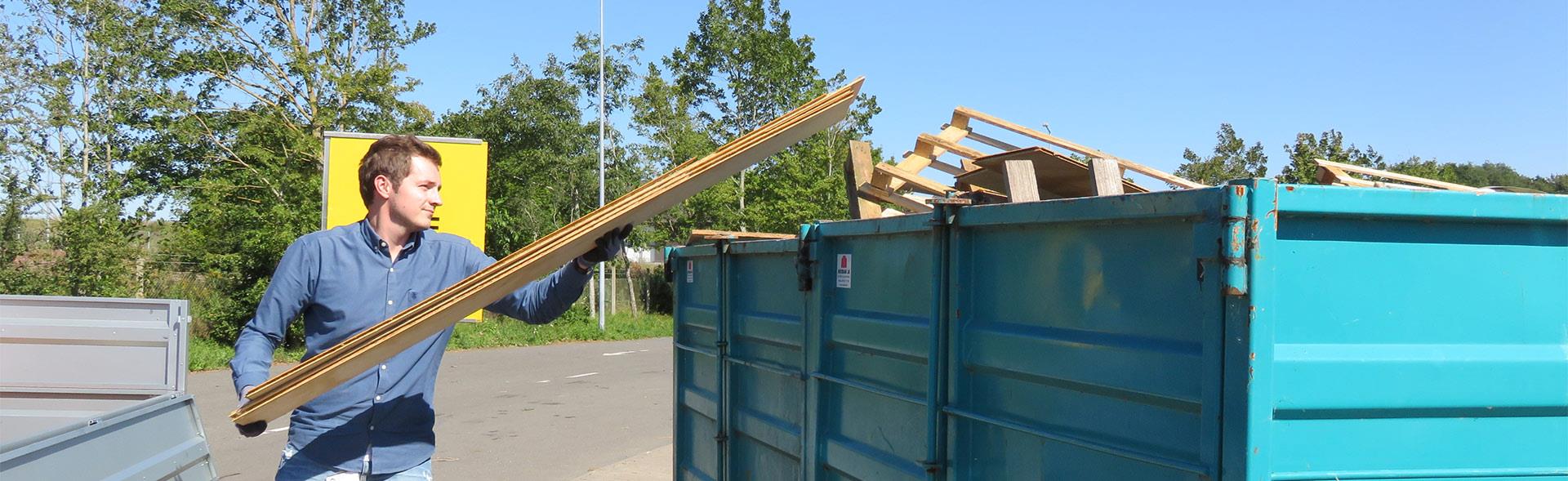 Mand smider brædder i container på genbrugsplads