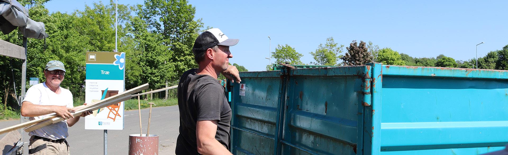 To håndværkere smider brædder op i container på genbrugsplads
