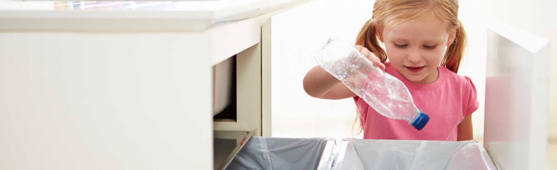 Pige sorterer en plastflaske til genbrug i affaldsspand i køkken