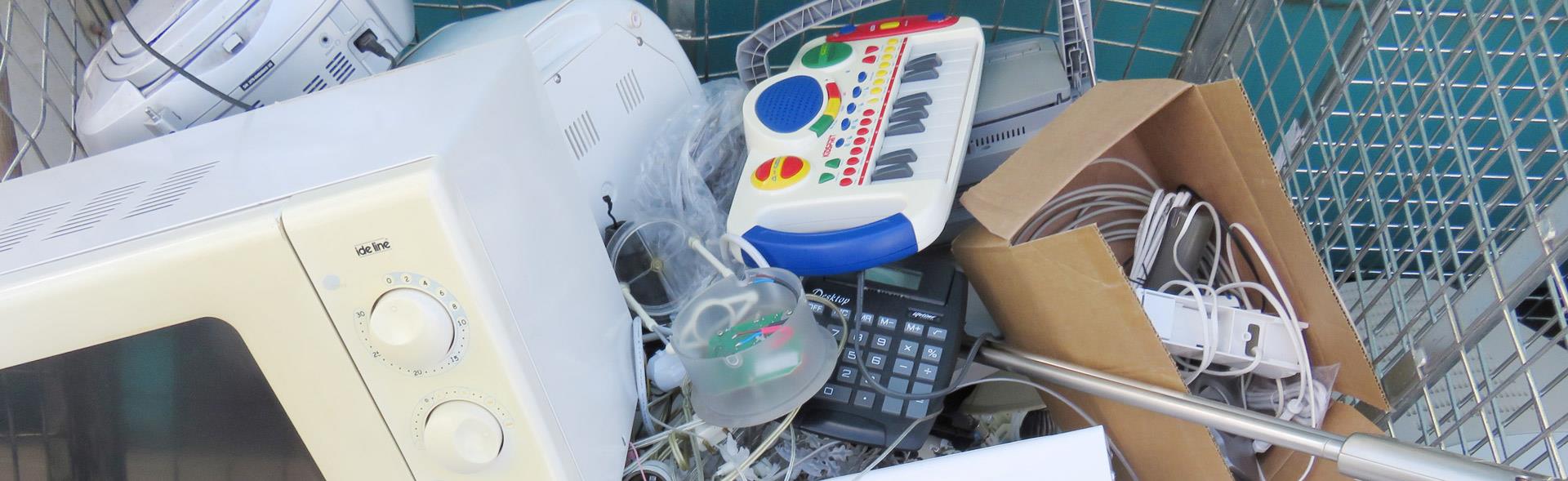 Microovn, legetøjskeyboard, ledninger og andet elektronik i bur på genbrugsplads