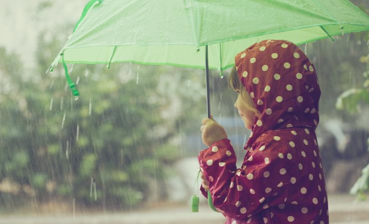 Pige med rød regnjakke står under grøn paraply