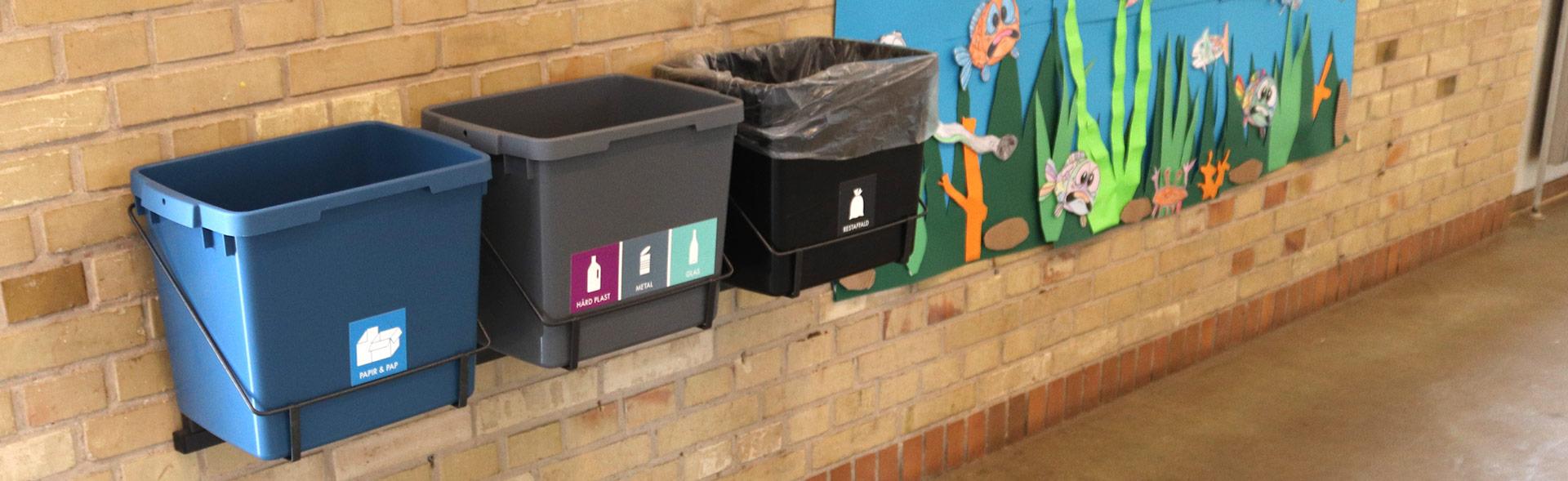 Tre spande til affaldssortering hænger på væg i skole