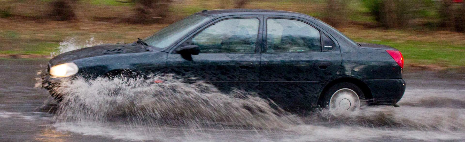 Bil kører på vej med enormt meget regnvand så det sprøjter ud til siderne