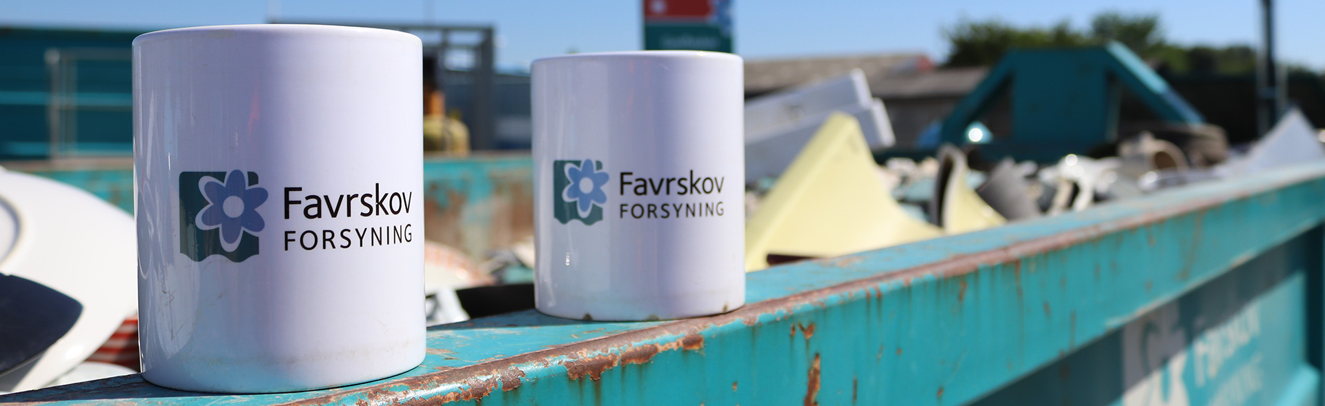 To kopper med Favrskov Forsyning logo står på container på på genbrugsplads
