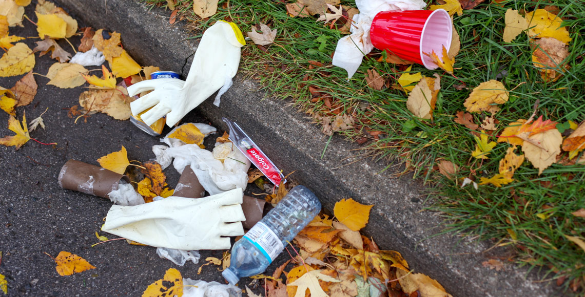 Henkastet affald ligger i kantsten, plastflaske, gummihandsker og andet