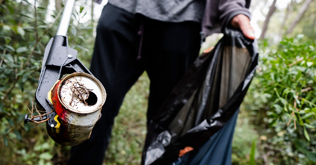 Person med en affaldstang samler en dåse op fra skovbunden
