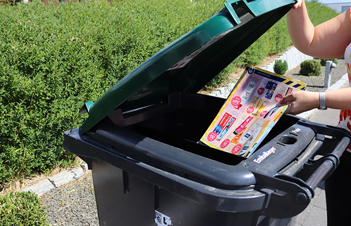 Person lægger reklamer af papir i beholder til affaldssortering