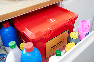 Rød kasse til farligt affald står i skuffe sammen med rengøringsmidler