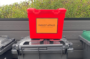 Rød kasse til farligt affald står på låget af en affaldsbeholder
