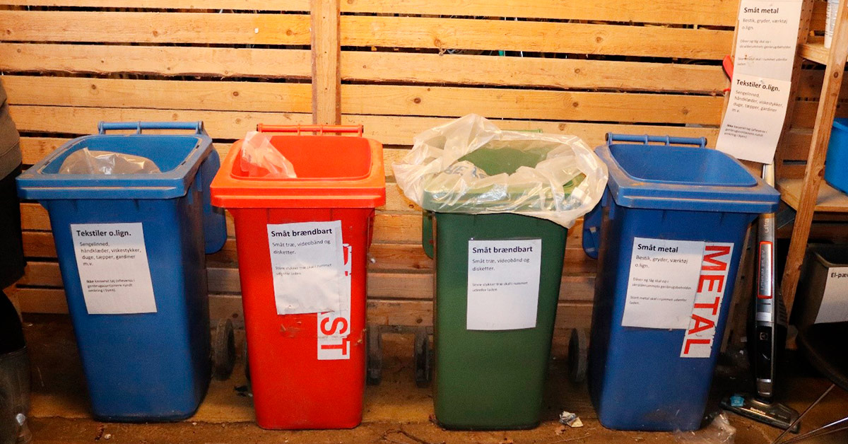 Affaldsbeholdere i forskellige farver står i skur