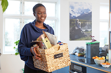 Kvinde står med kurv, der er fyldt op med papir og pap til sortering