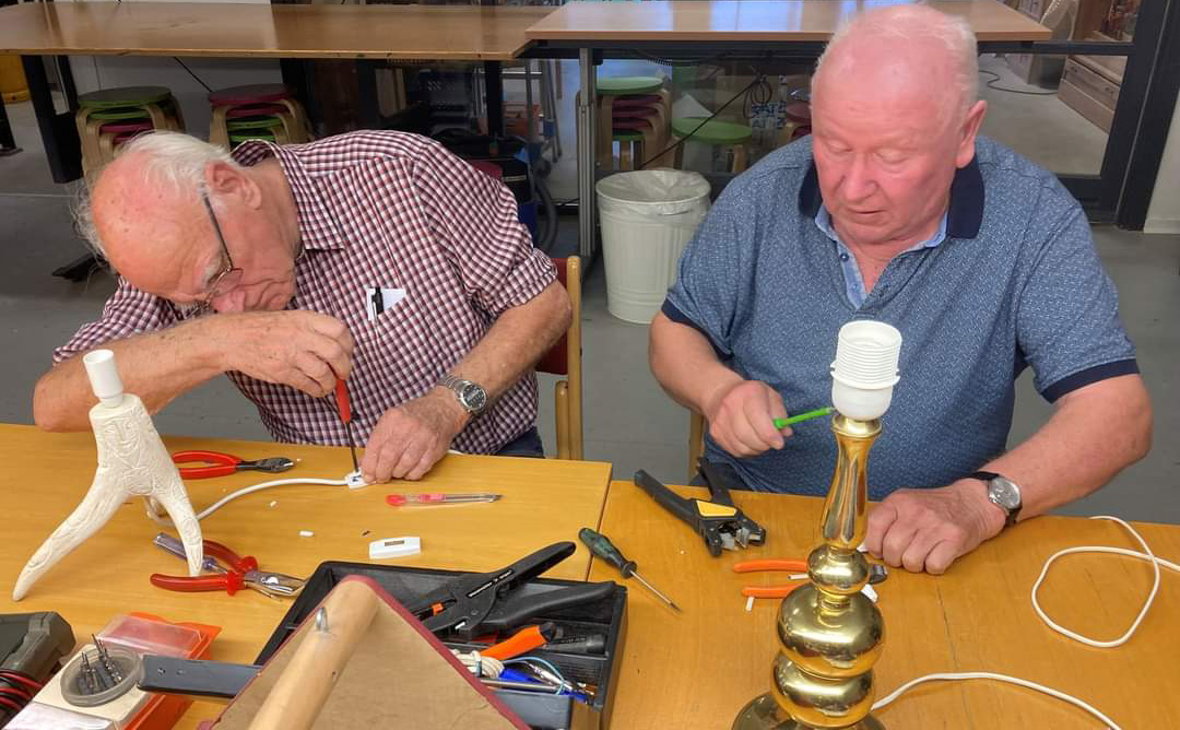 To herre sidde ved bord og reparerer elektronik